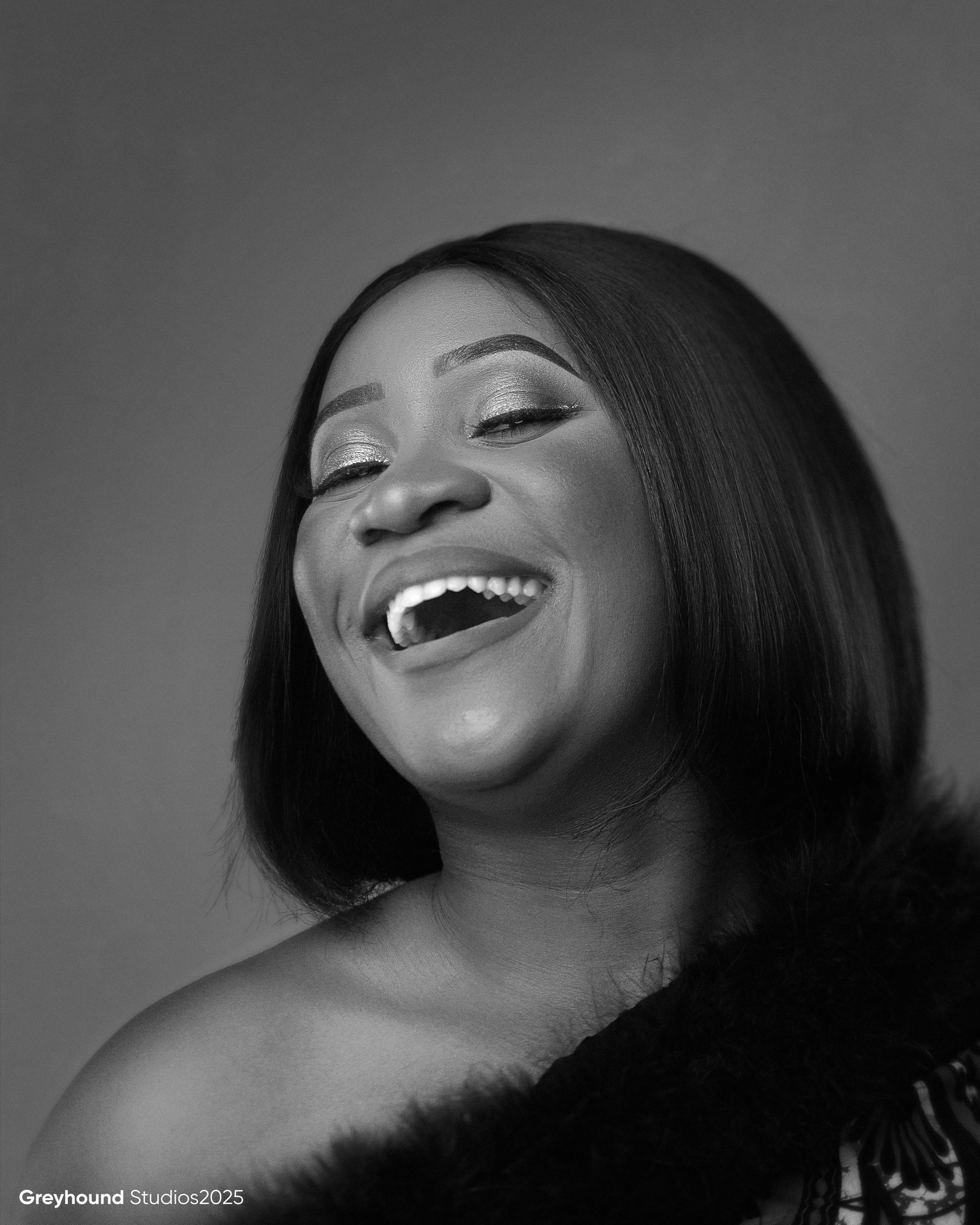 Black and white portrait of Tendai Makoni laughing joyfully in African print dress with fur trim